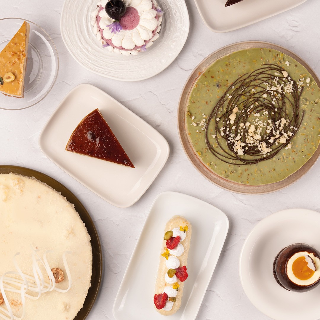 Vista superior de sobremesas variadas, incluindo cheesecake, pudim, tarte de pistache, éclair e mousse de chocolate e...